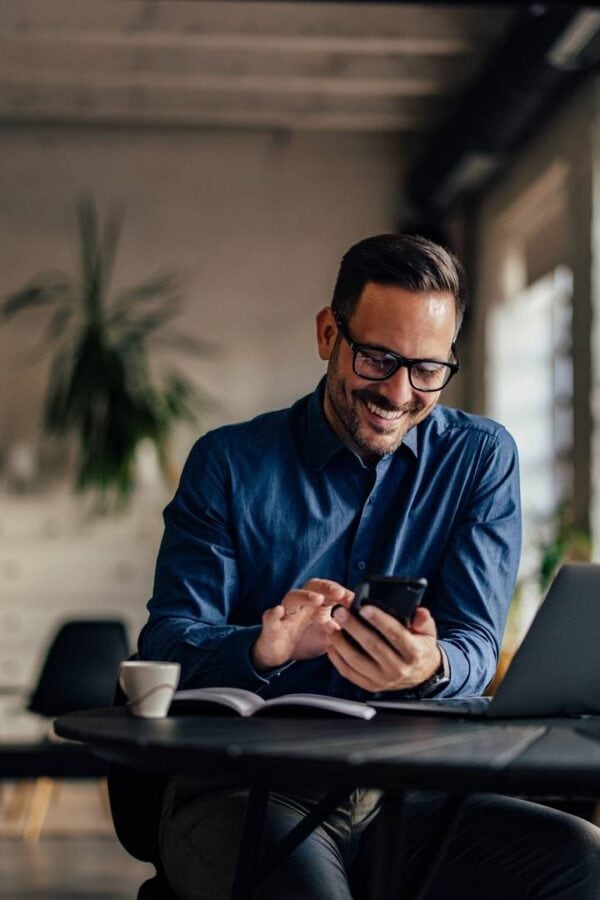 Profesjonalista uśmiechający się podczas korzystania ze smartfona biznesowego premium przy laptopie – inwestycja w wydajny flagowiec dla firmy