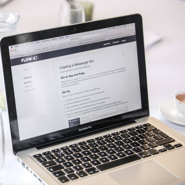 Close-up of a MacBook Pro displaying a webpage, with coffee cups and water pitcher on a table.