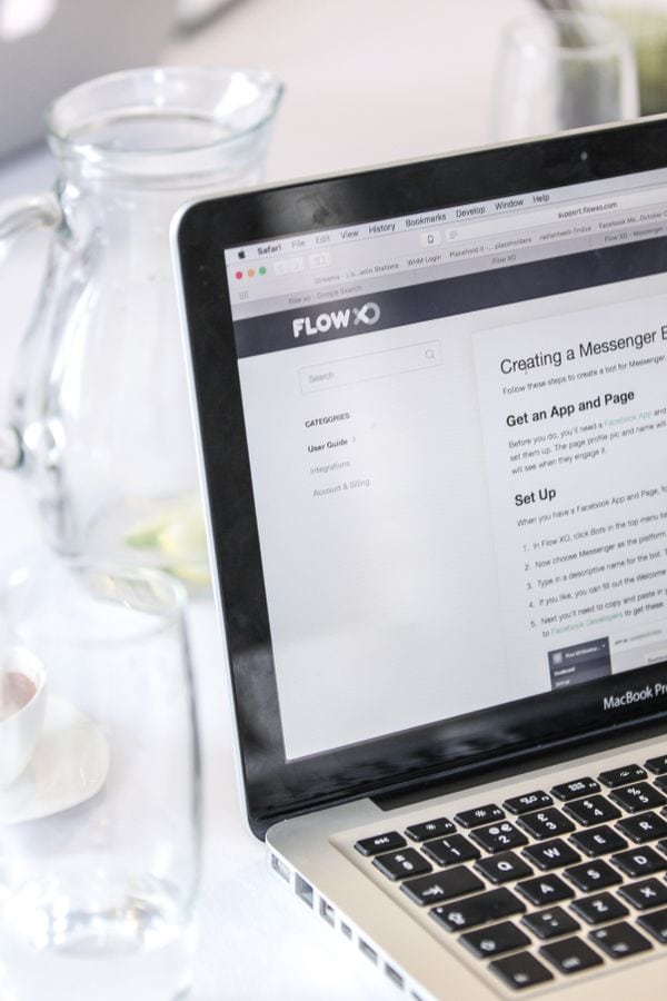 Close-up of a MacBook Pro displaying a webpage, with coffee cups and water pitcher on a table.