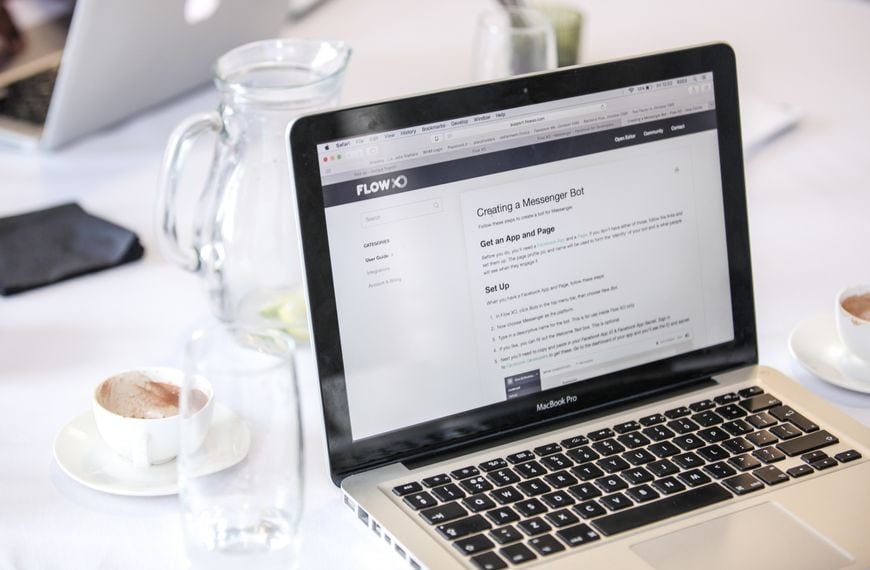 Close-up of a MacBook Pro displaying a webpage, with coffee cups and water pitcher on a table.